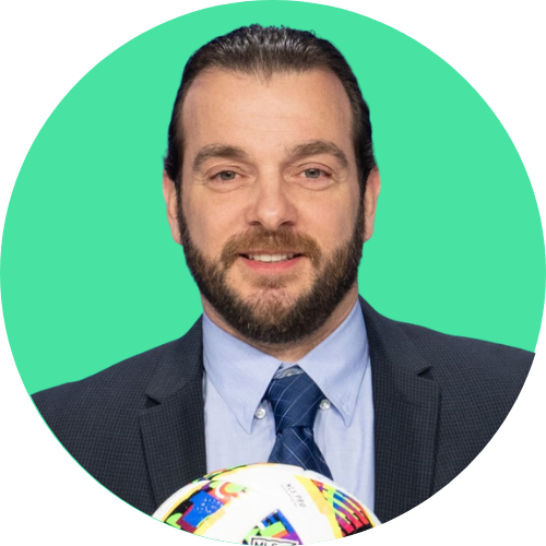 Professional man in a navy suit and blue tie, smiling, with a soccer ball at the bottom edge against a bright green circular background.